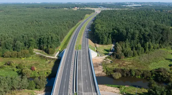 Widok z lotu ptaka na autostradę A1 otoczoną lasem, z mostem nad rzeką.