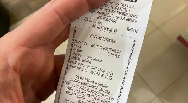 Dłoń trzyma paragon z napisem "BILET AUTOSTRADOWY" i logo ORLEN.